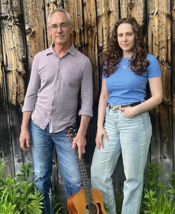 Paul and Danielle of Borrow the Bones leaning on a weathered barn wall